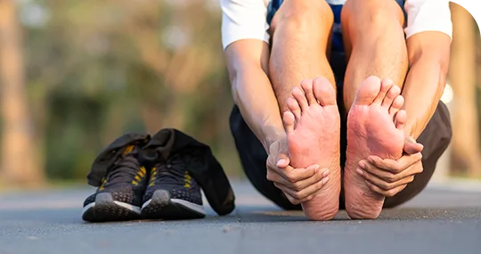 Corredor descalzo sujetándose las plantas de los pies enrojecidas junto a sus tenis
